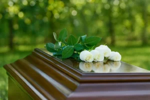 Roses blanches posées sur un cercueil en bois verni lors d'une cérémonie d'obsèques en extérieur.